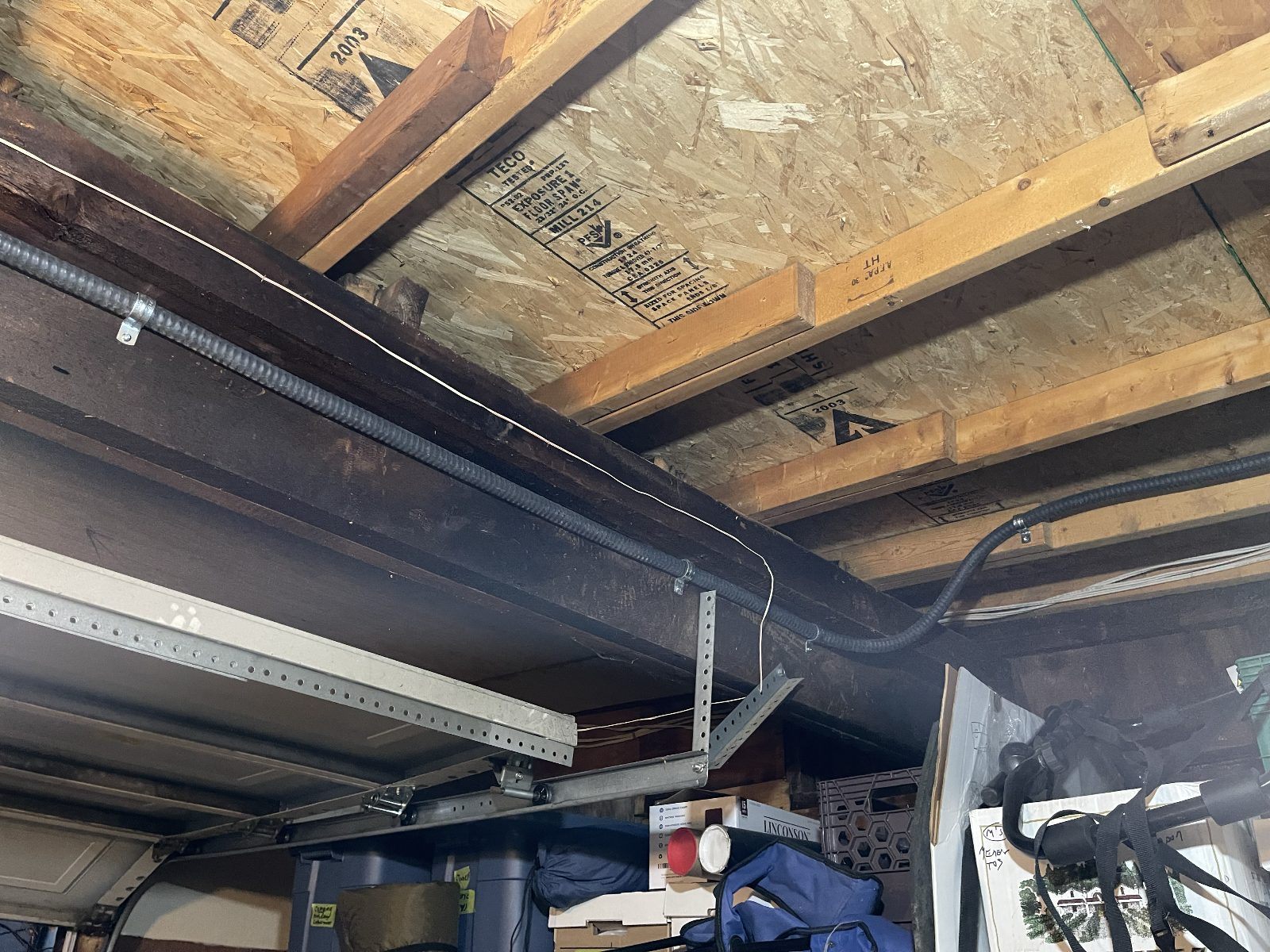 Feed routed through the joist bay and supported on strut — straight, level, and out of the way of garage door tracks.