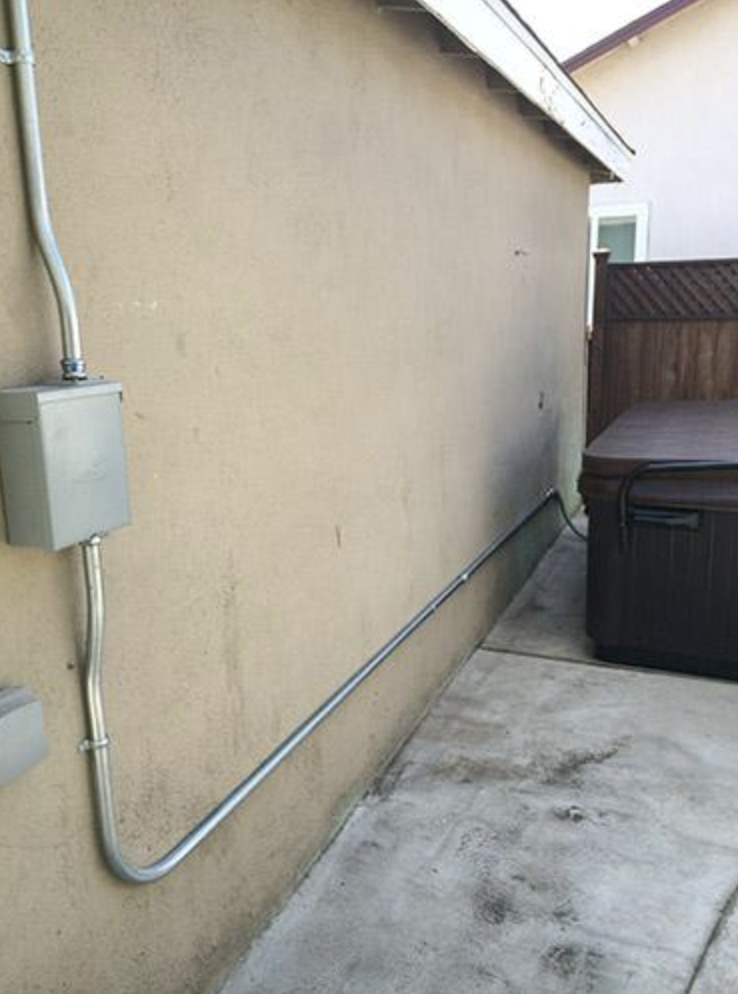 Clean conduit run from the panel along the side of the house to the hot tub disconnect — properly strapped, straight pulls, no sag.