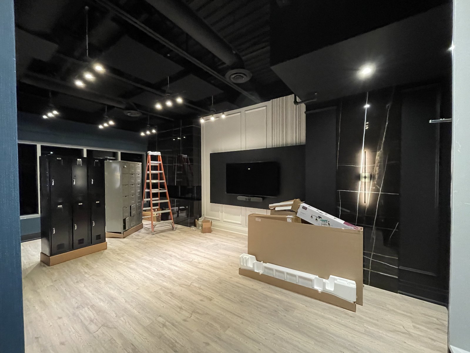Member lounge — slatted feature wall, recessed downlights on dimmer scenes, dedicated AV circuits behind the wall-mount TV.